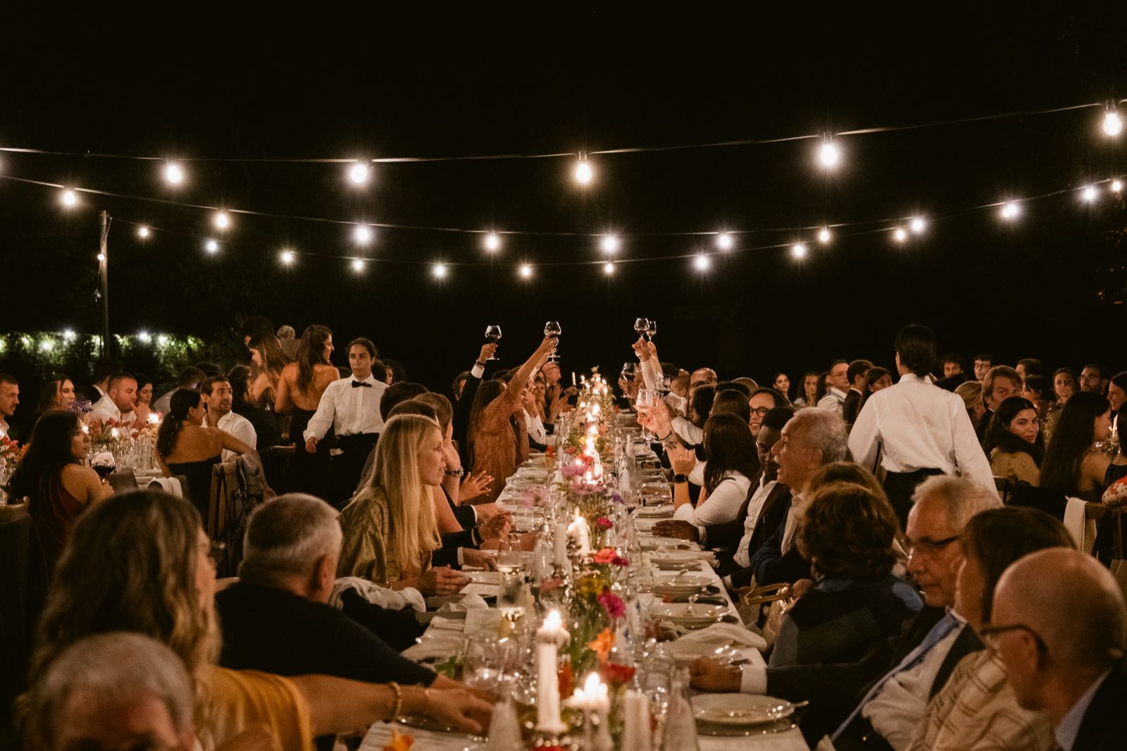 Raising a toast at the table in the evening, beneath the string lights