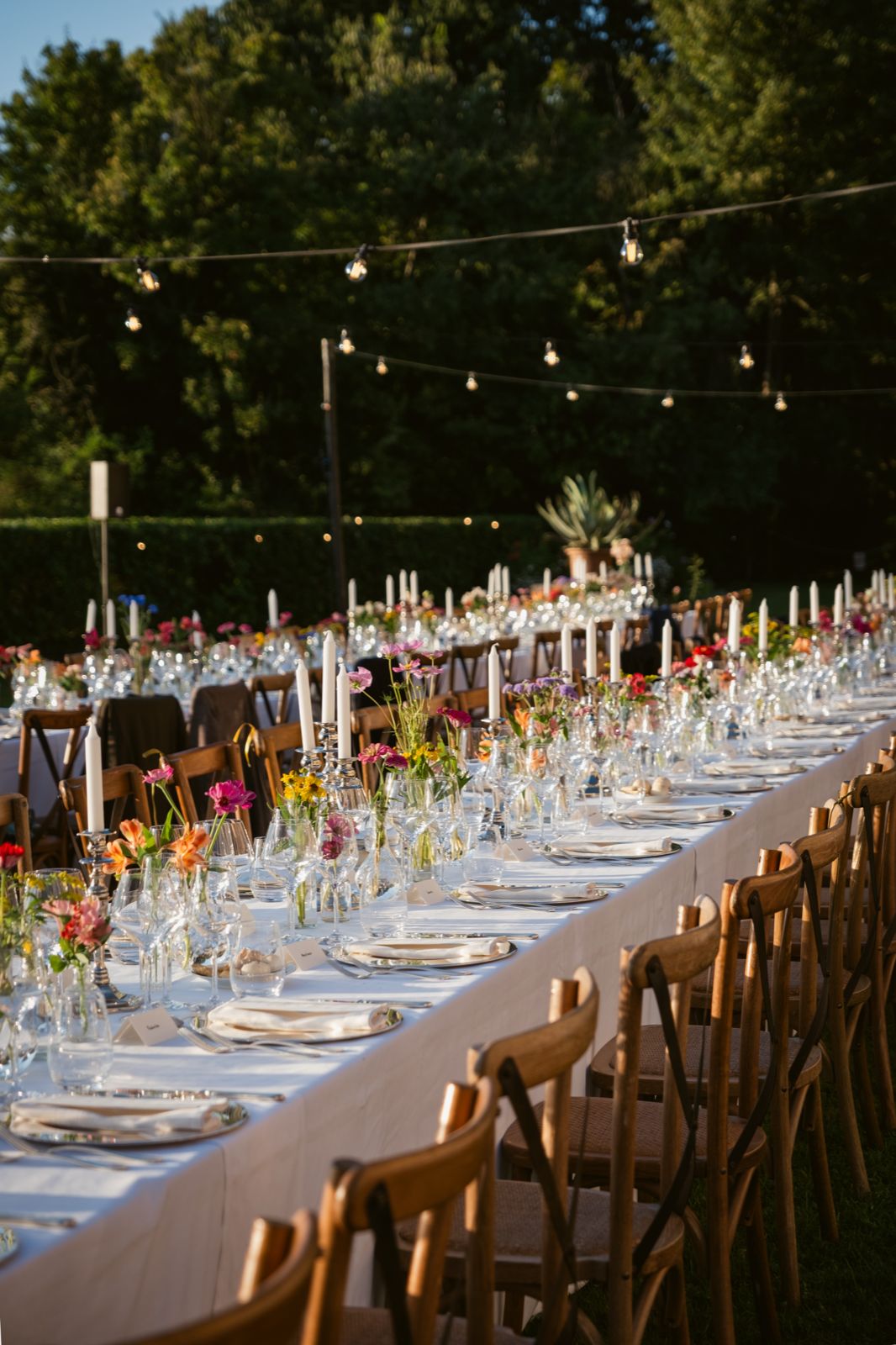 The long table on the lawn beneath strings of lights, candles lit